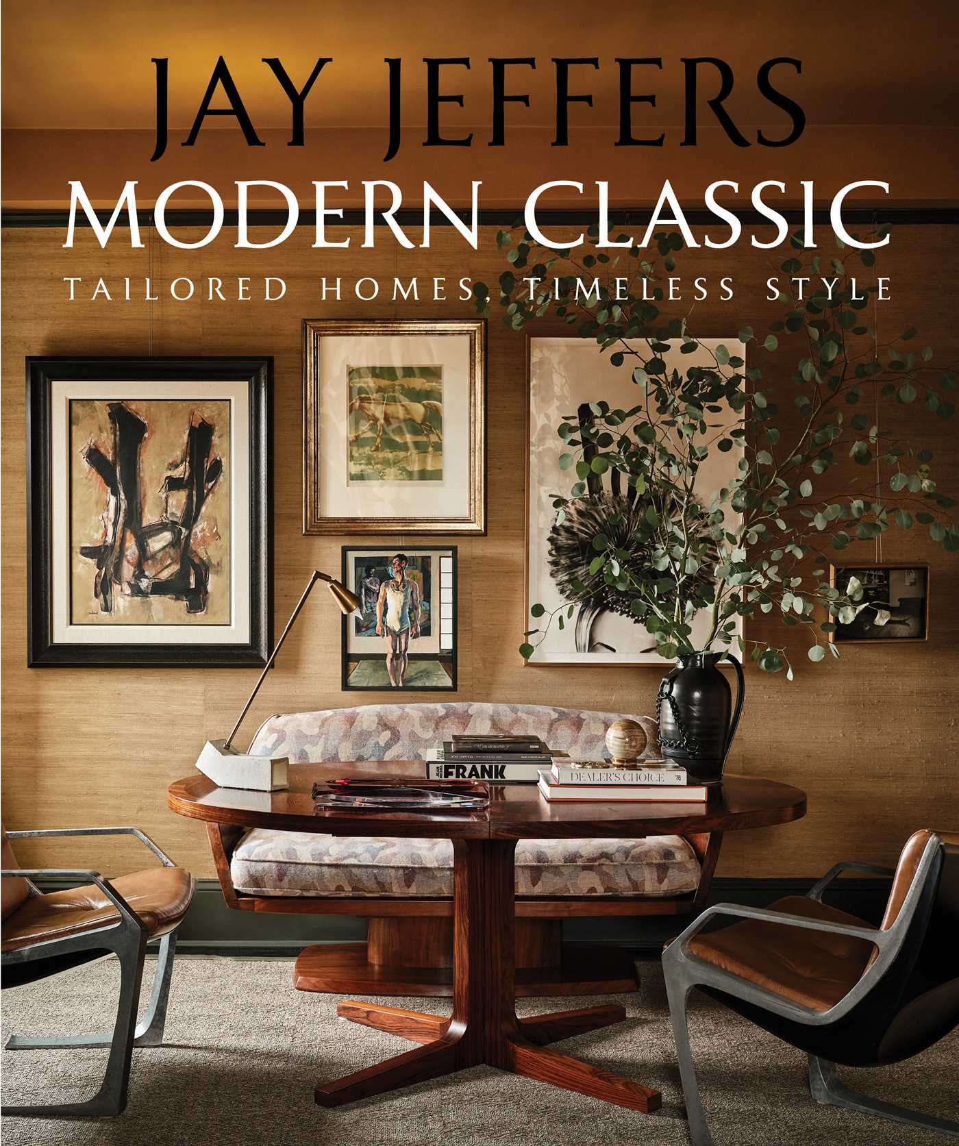 A stylish living room features a wood table, patterned sofa, leather chairs, framed abstract art on textured walls, books, a lamp, and a tall vase with green branches. Overlay text reads: Jay Jeffers Modern Classic: Tailored Homes, Timeless Style.